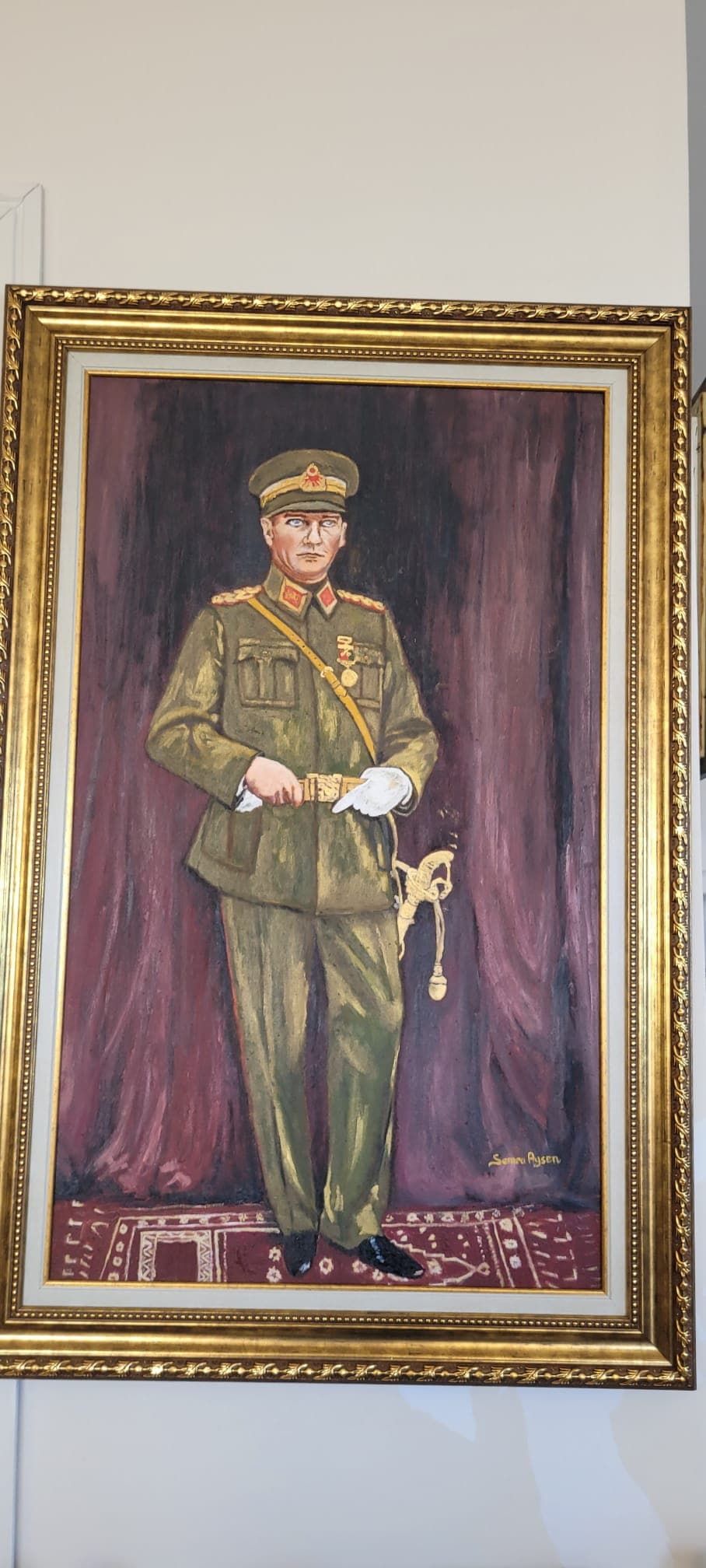 Ölgemälde von Mustafa Kemal Atatürk in grüner Militäruniform mit Säbel vor einem lila Vorhang.
